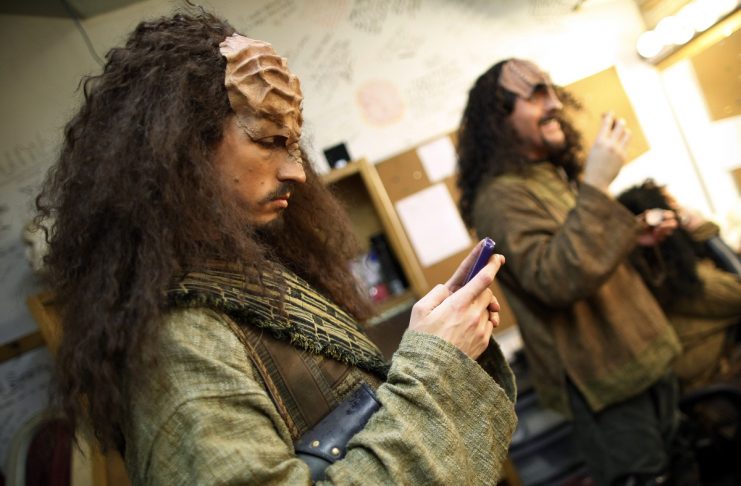 Performer Jon Beal checks his email as Josh Zagoren puts on his make-up for a performance in “A Klingon Christmas Carol” in Chicago