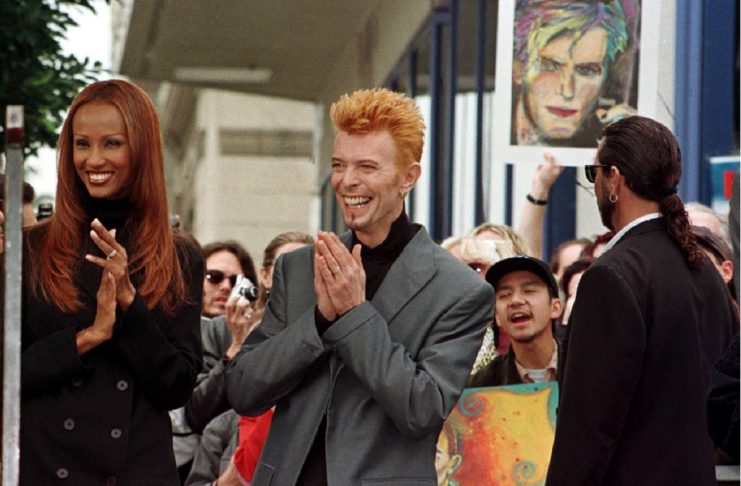 Rock singer David Bowie (R) is shown with his wife Iman (L) with a crowd of Bowie’s fans behind them..