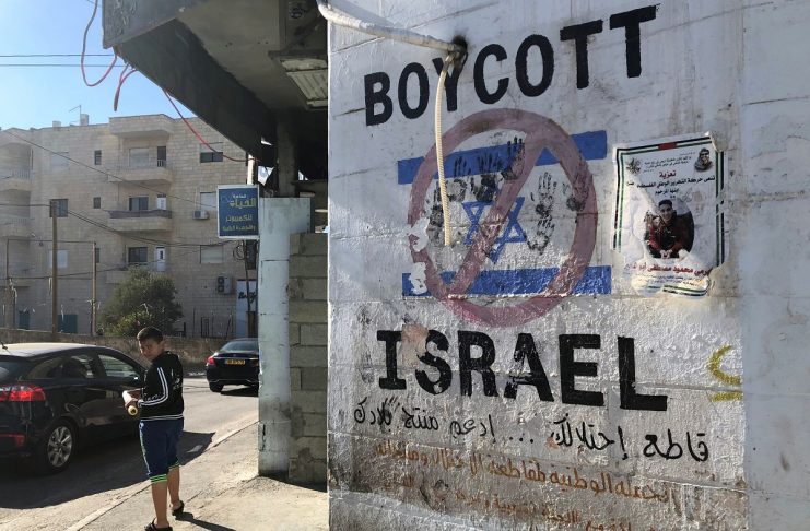 Palestinian boy looks on as a graffiti on boycotting Israel is seen on a wall in Bethlehem in the Israeli-occupied West Bank