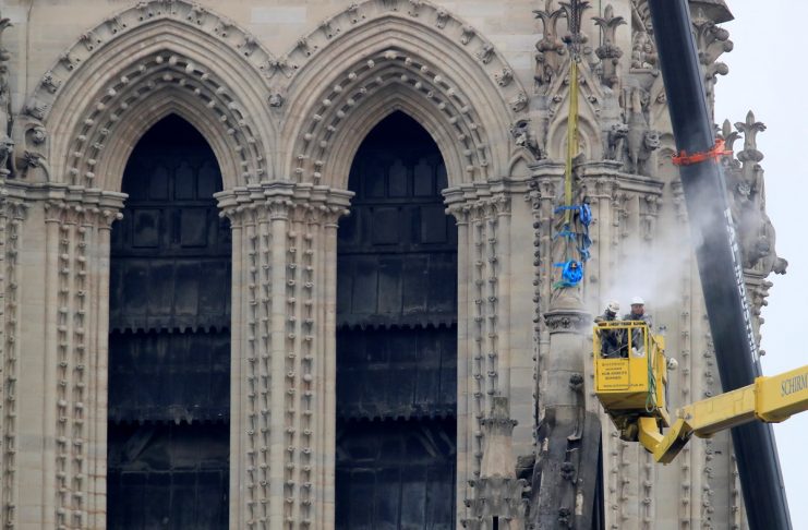 Men work on a statue at Notre-Dame Cathedral after a massive fire devastated large parts of the gothic structure in Paris